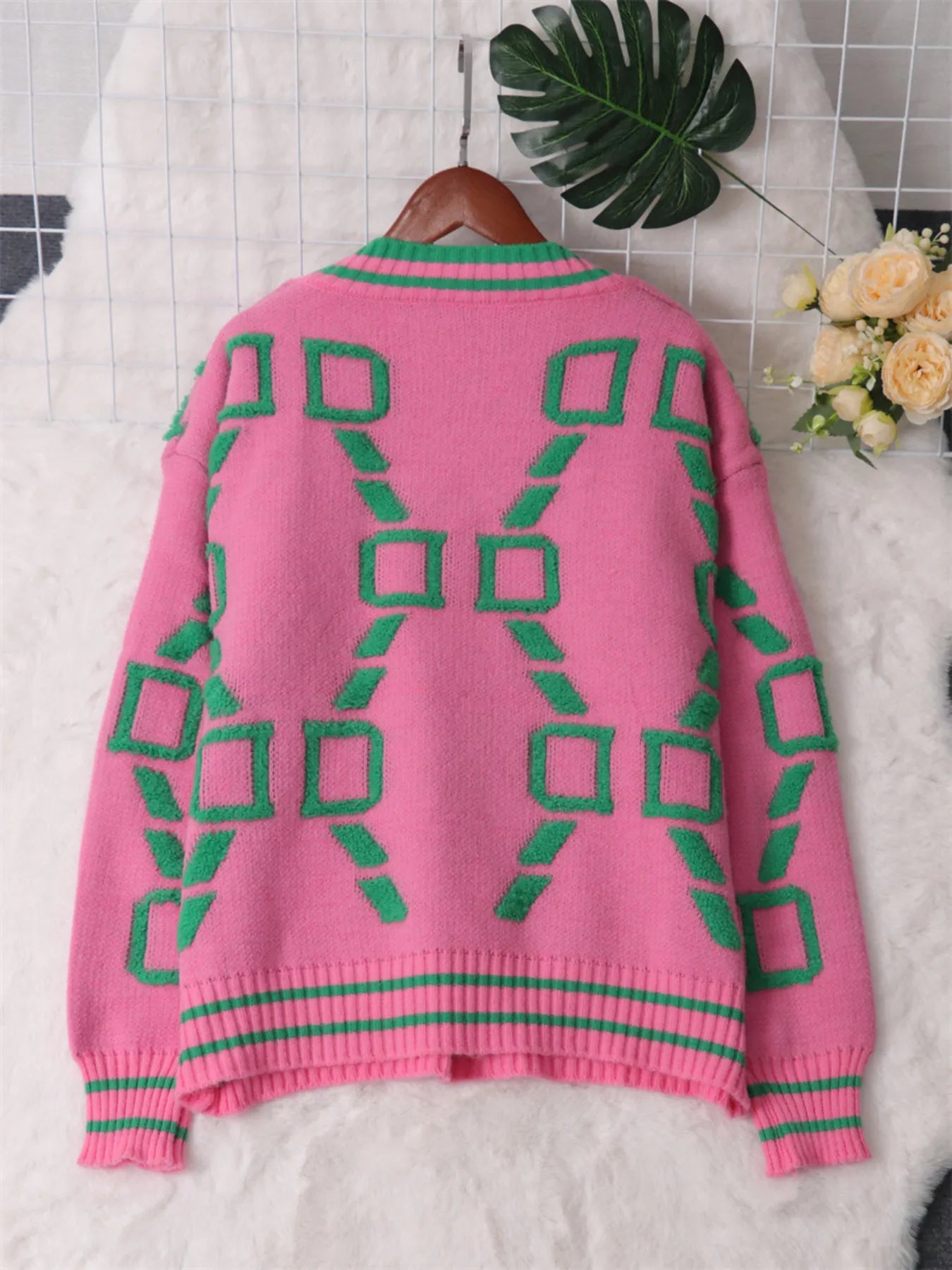 Pink knit sweater laid flat with green geometric square pattern and ribbed hem