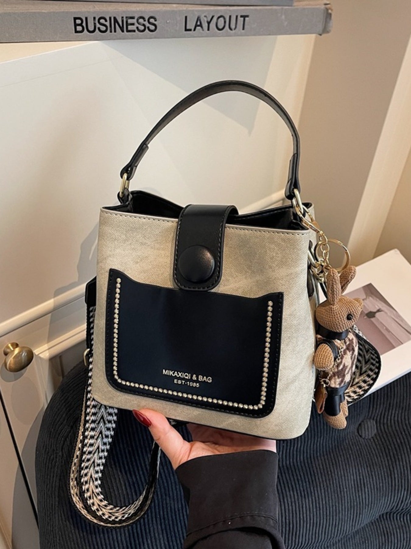 Two-Tone bucket crossbody bag by Trendsi; small beige PU bag with black front pocket and studded trim.