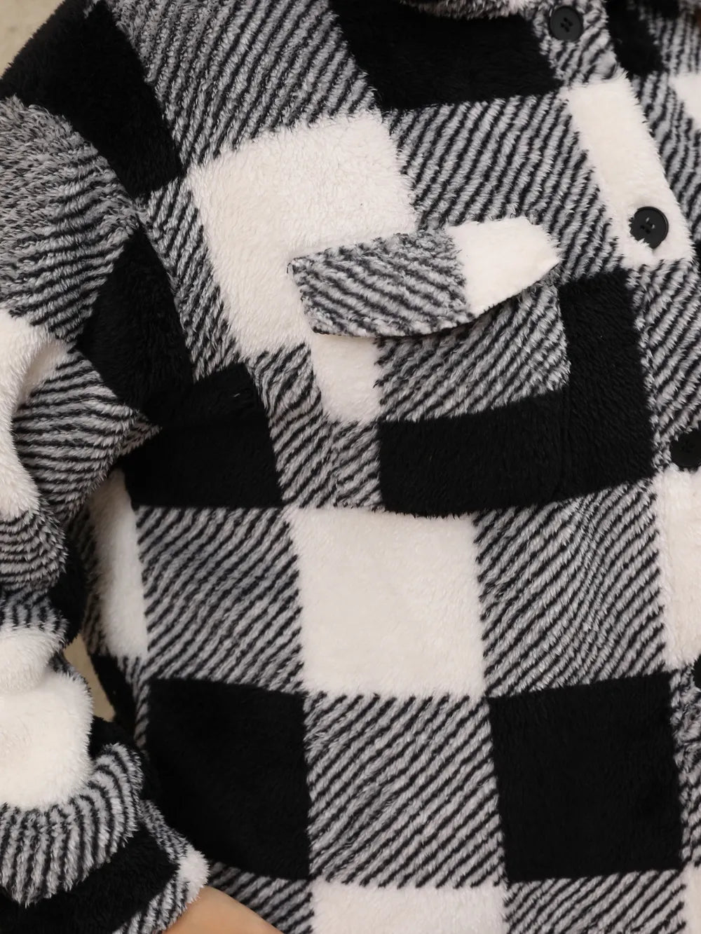 Black-and-white plaid jacket fabric close-up with buttoned flap pocket