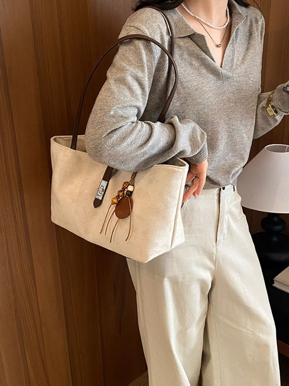 Beige suede shoulder tote with buckle detail strap and small tassel charm