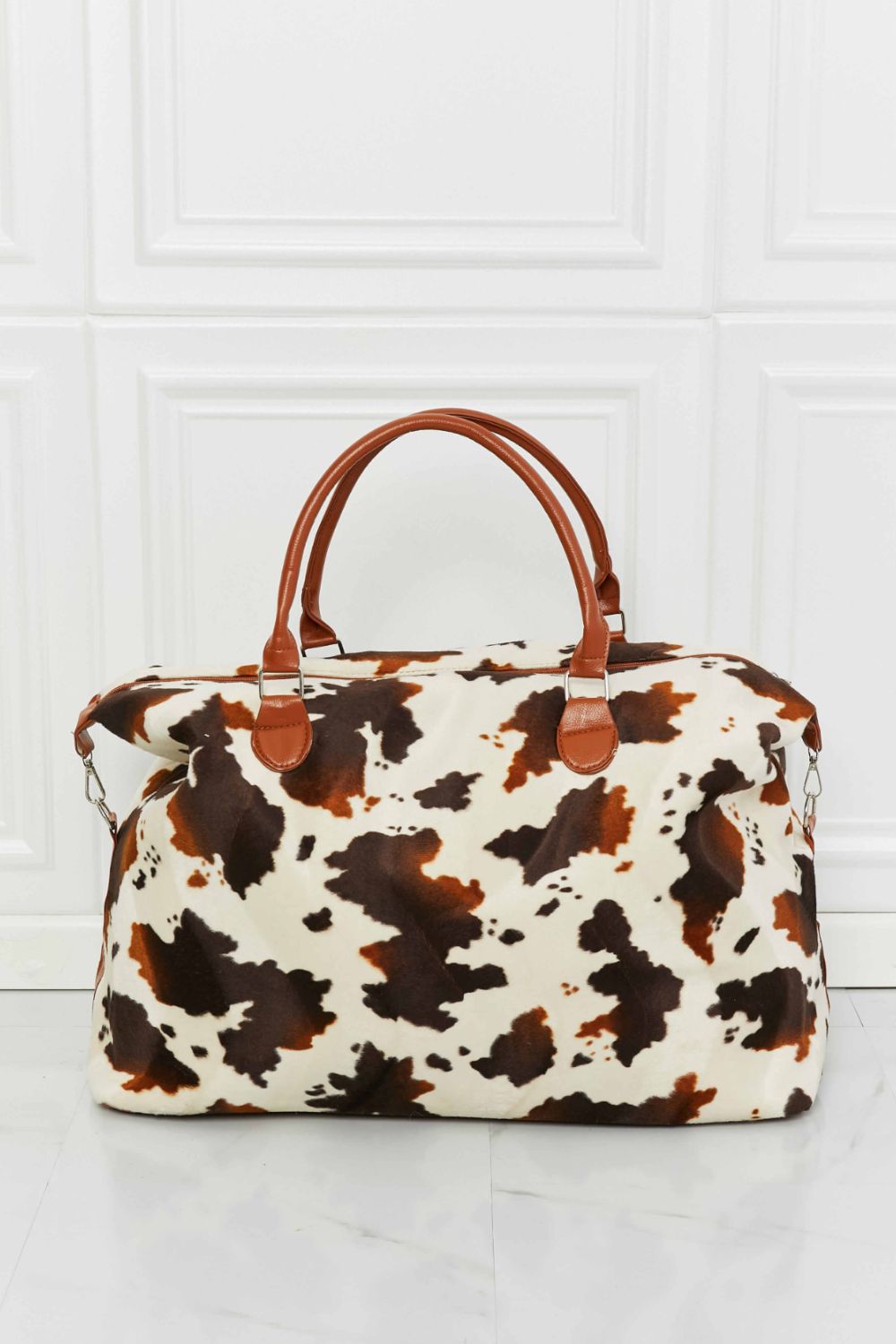 Cow print plush weekender bag with tan handles and white-and-brown patch pattern