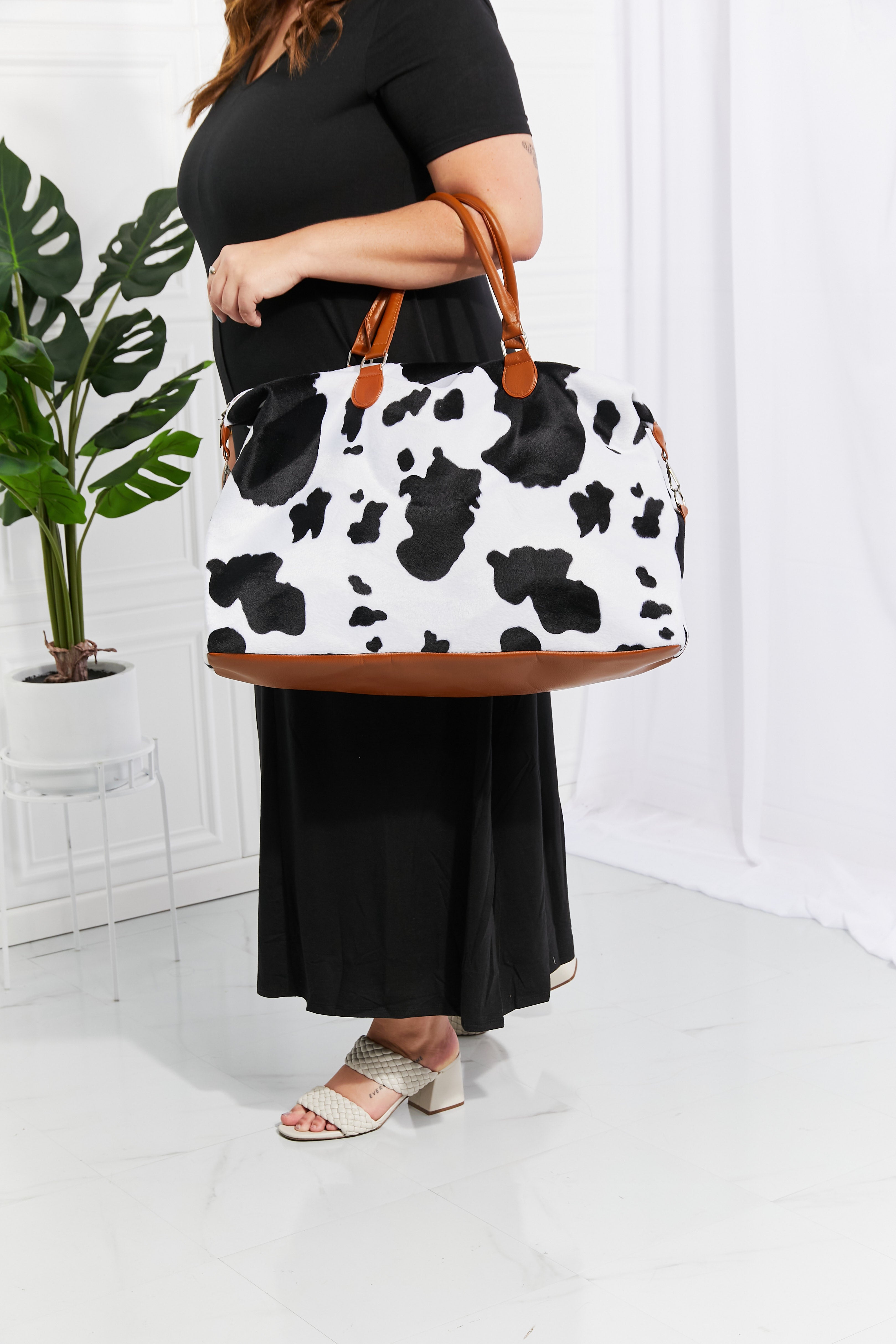 Cow print plush weekender bag with tan handles and roomy zip-top opening
