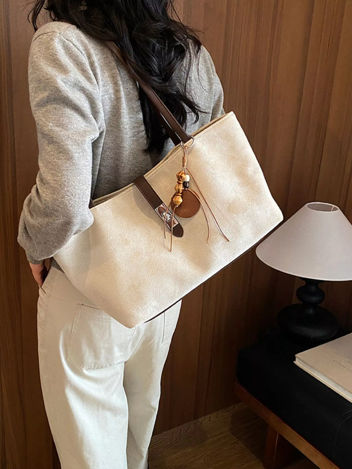Beige suede medium tote bag worn on shoulder, showing buckle strap and charms