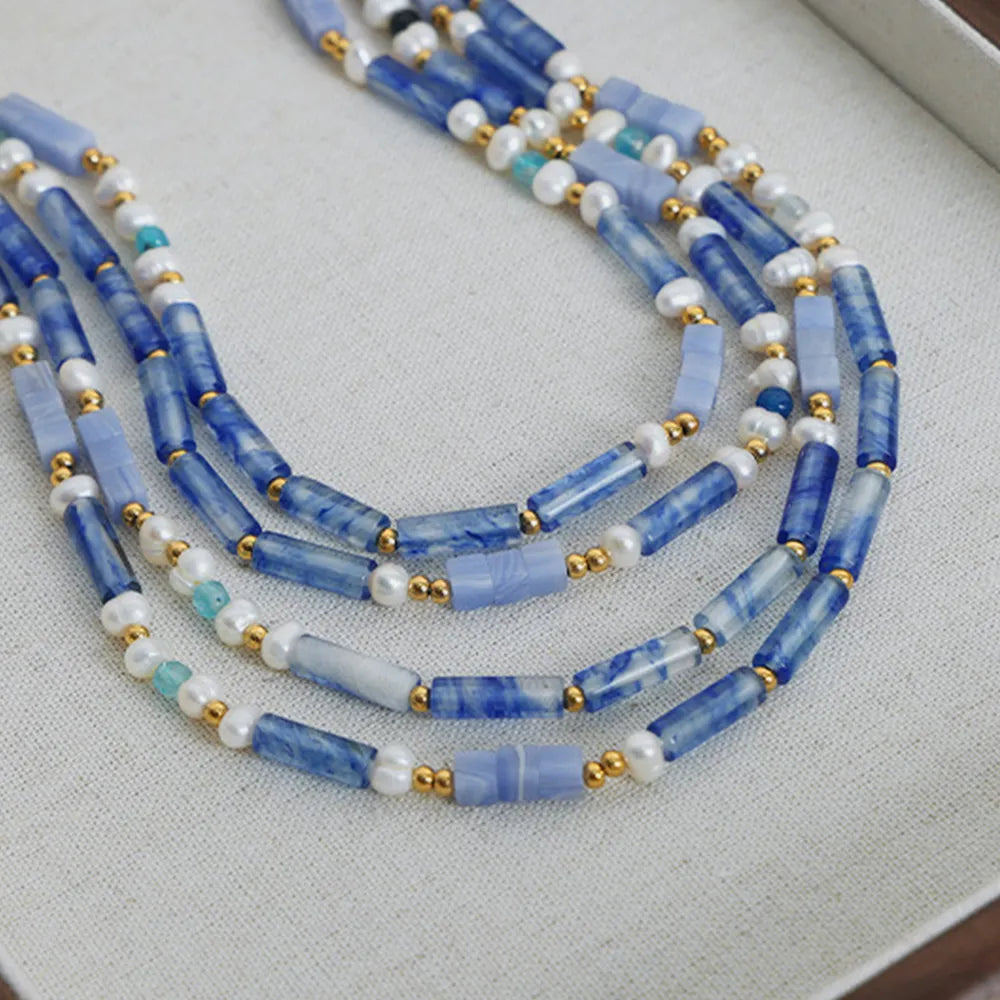 Multi-strand blue bead necklace with freshwater pearls, gold accents, and light green beads