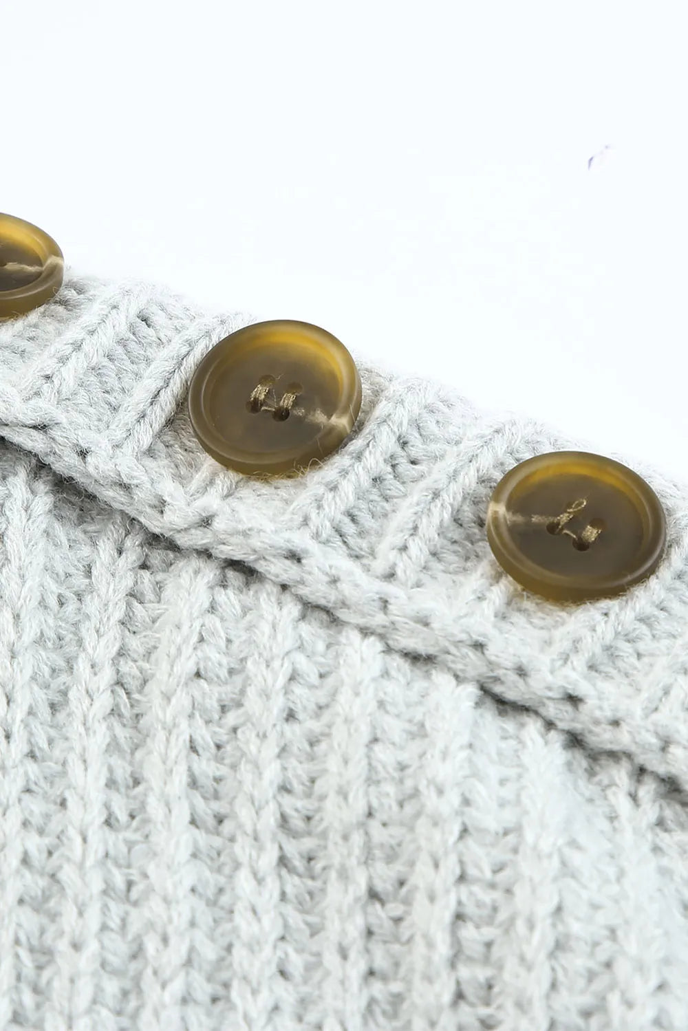 Close-up of light gray knit sweater with round gold buttons on shoulder trim