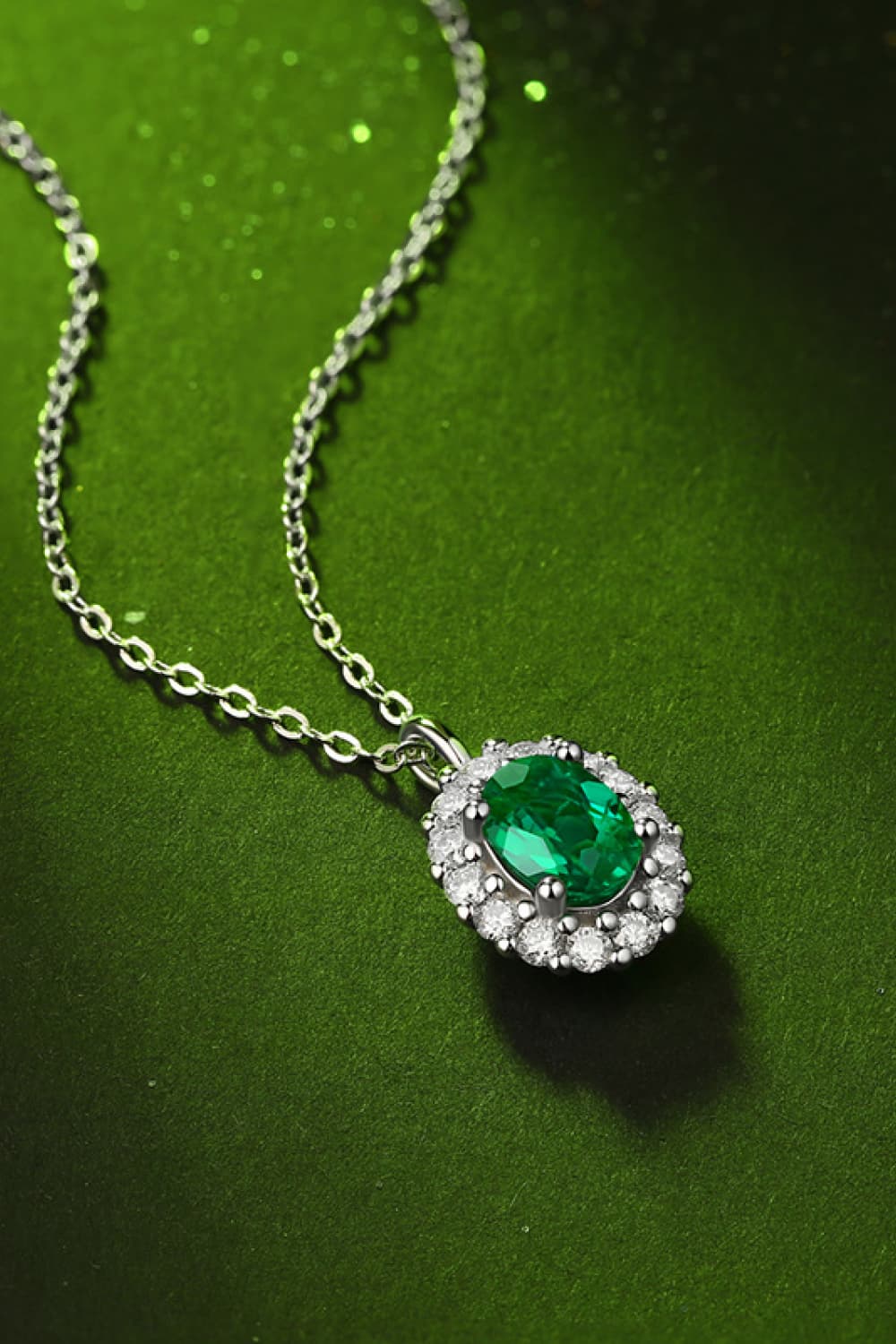 Sterling silver necklace with green emerald halo pendant, side angle on chain