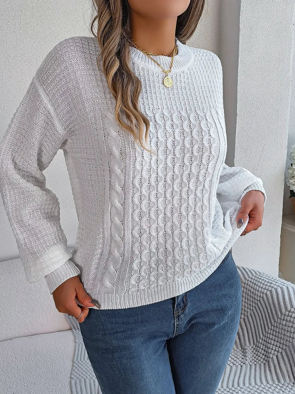 White cable-knit long sleeve sweater with round neck and raised cable texture.