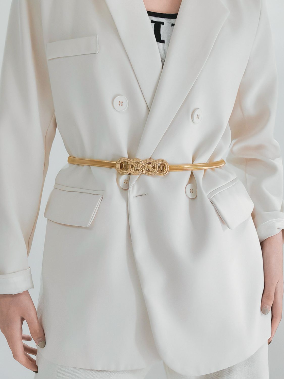 Gold-tone metal knot buckle belt on a light blazer, worn at the waist