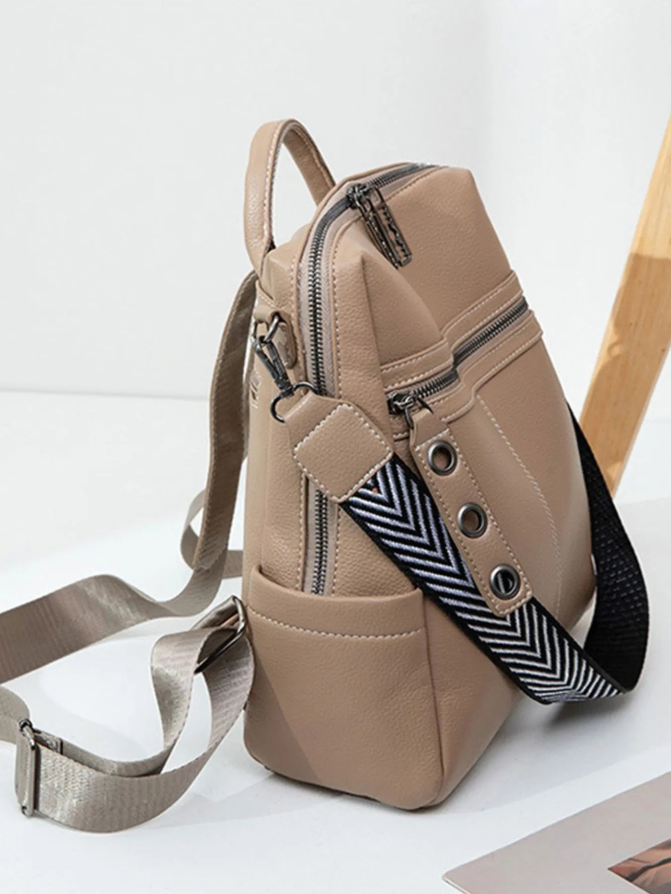 Beige leather backpack bag with side zipper pocket, chevron strap trim, crossbody carry