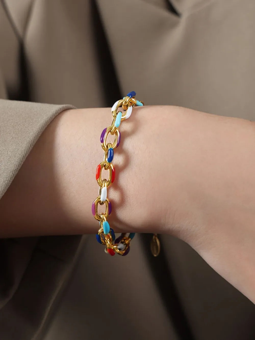 Multicolor chain bracelet on wrist with gold-toned links and blue red accents