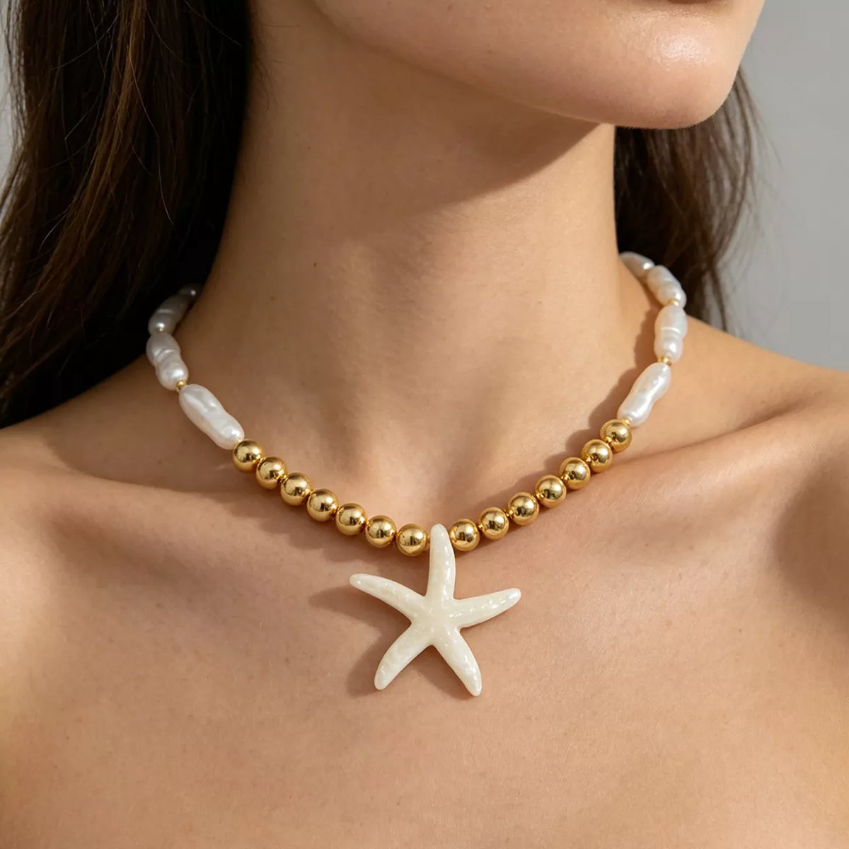 Gold-tone bead strand necklace with white starfish pendant over pearl-look beads