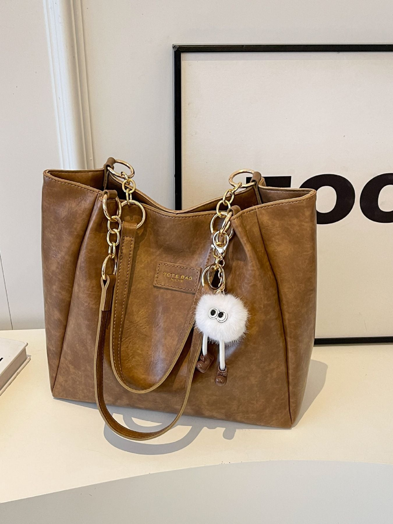 Chain Decor Leather Shoulder Bag in brown PU with gold chain handles and white fluffy pom-pom charm
