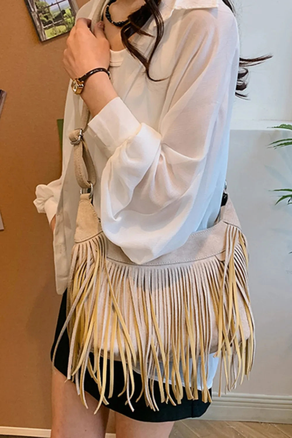 Light beige suede fringe shoulder bag worn with adjustable strap and top tassels