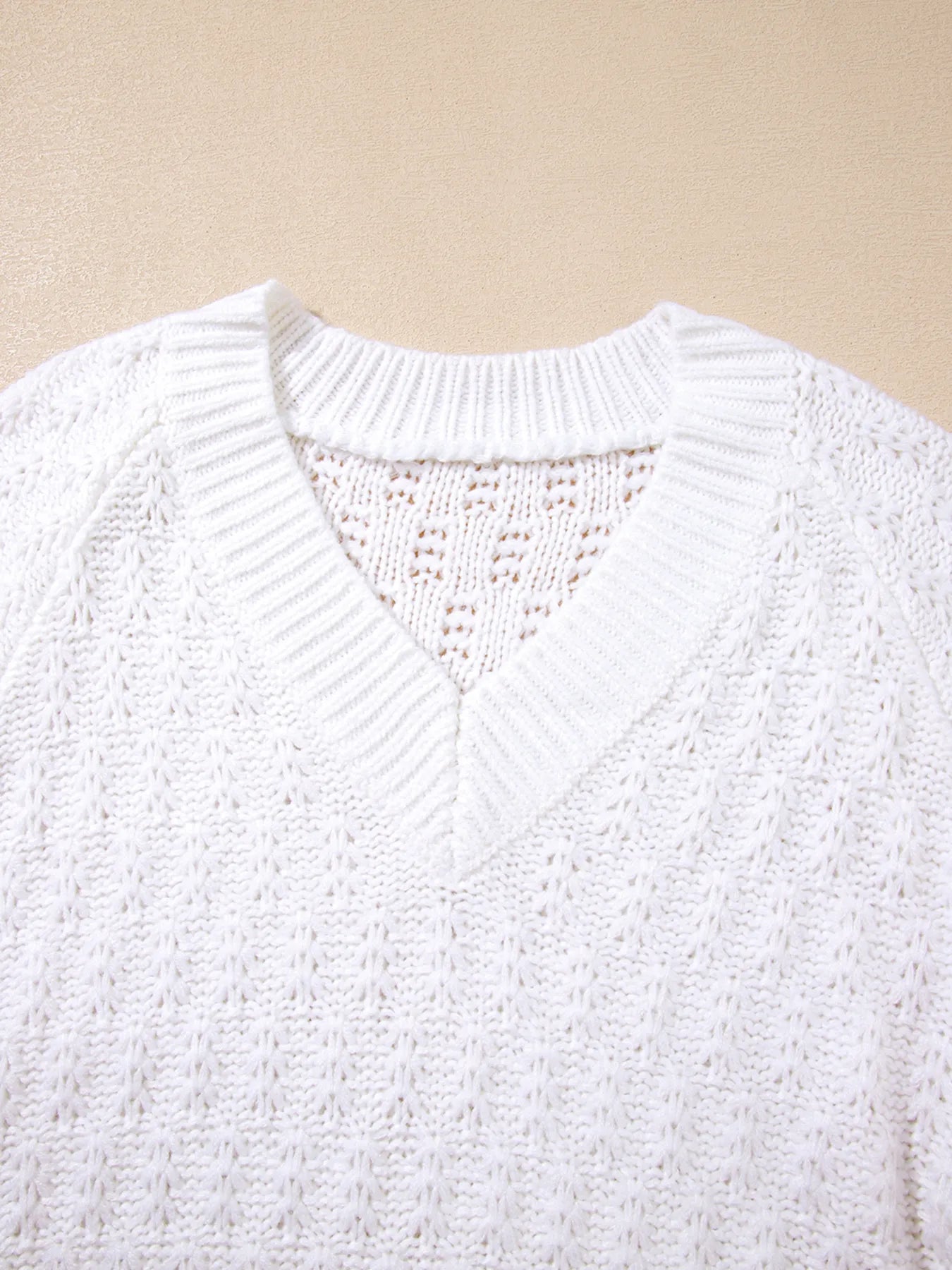 White textured knit V-neck sweater close-up with ribbed neckline and stitch pattern.