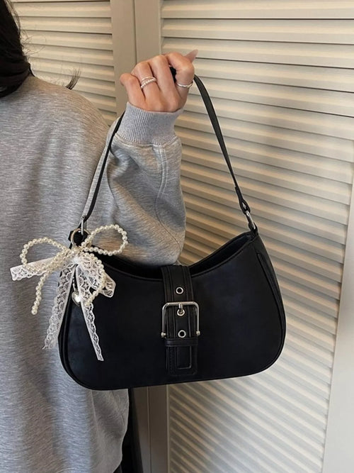 Black shoulder bag with front buckle strap and lace bow charm on shoulder