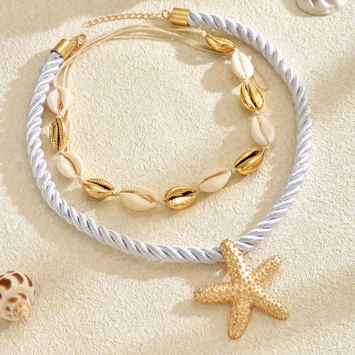 Gold starfish rope necklace with white shell beads and braided cord, flat lay view