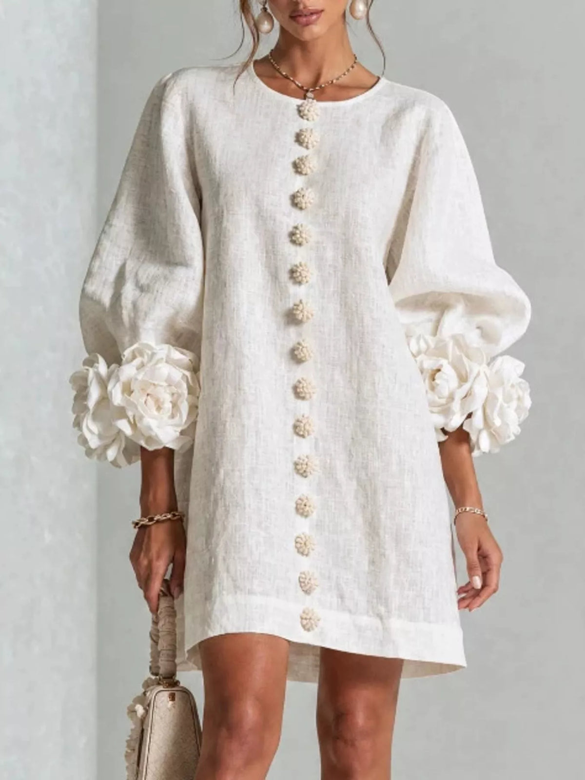 White mini dress with round neck, vertical button trim, and 3D floral puff sleeves.