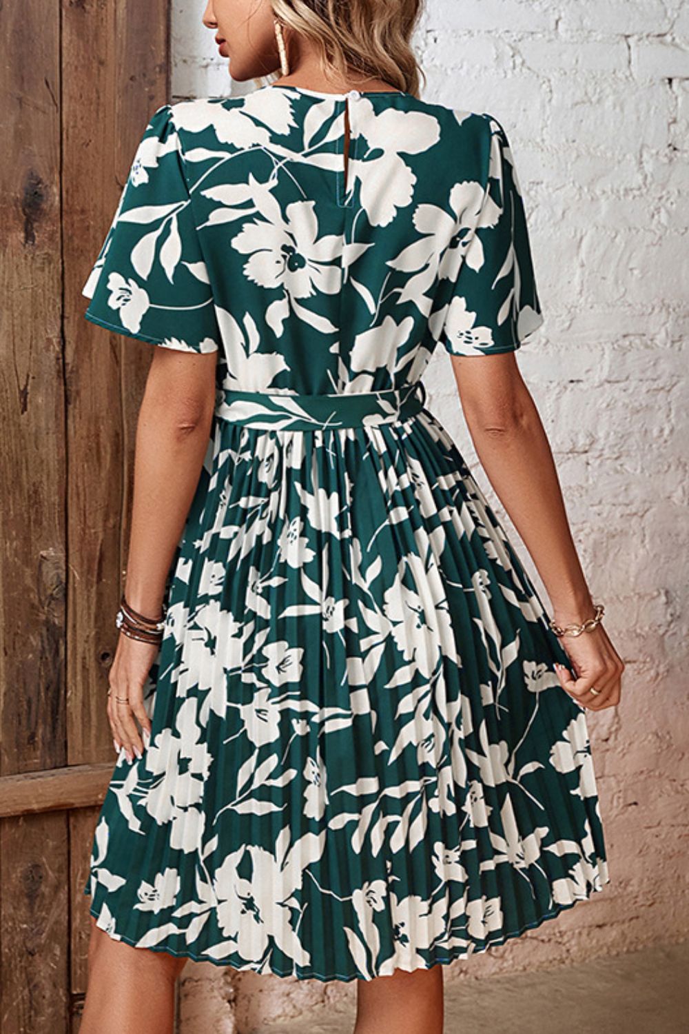 Back view of forest green floral pleated dress with tied waist and short sleeves