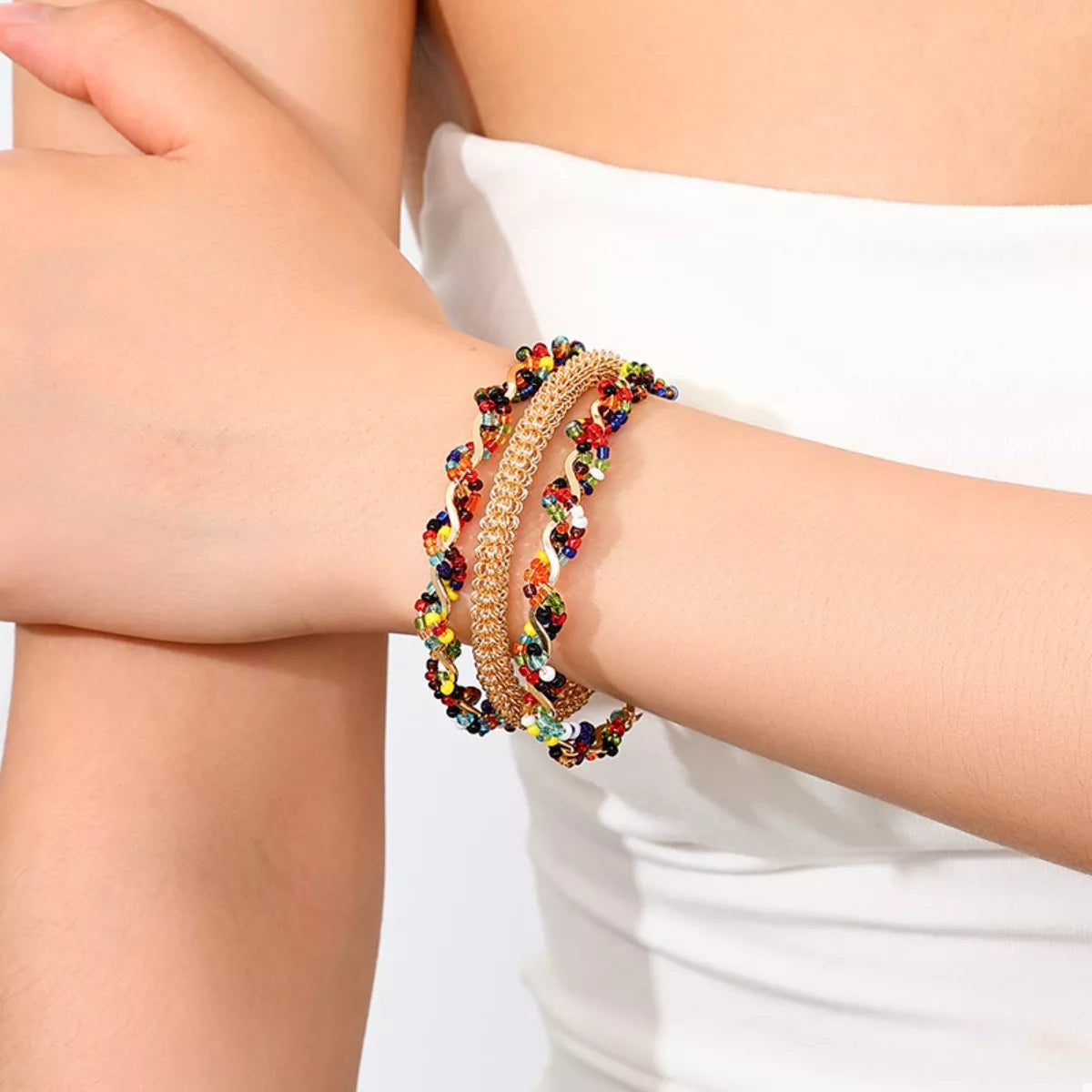 Gold open bracelet with three chain rows and colorful bead accents, worn on wrist